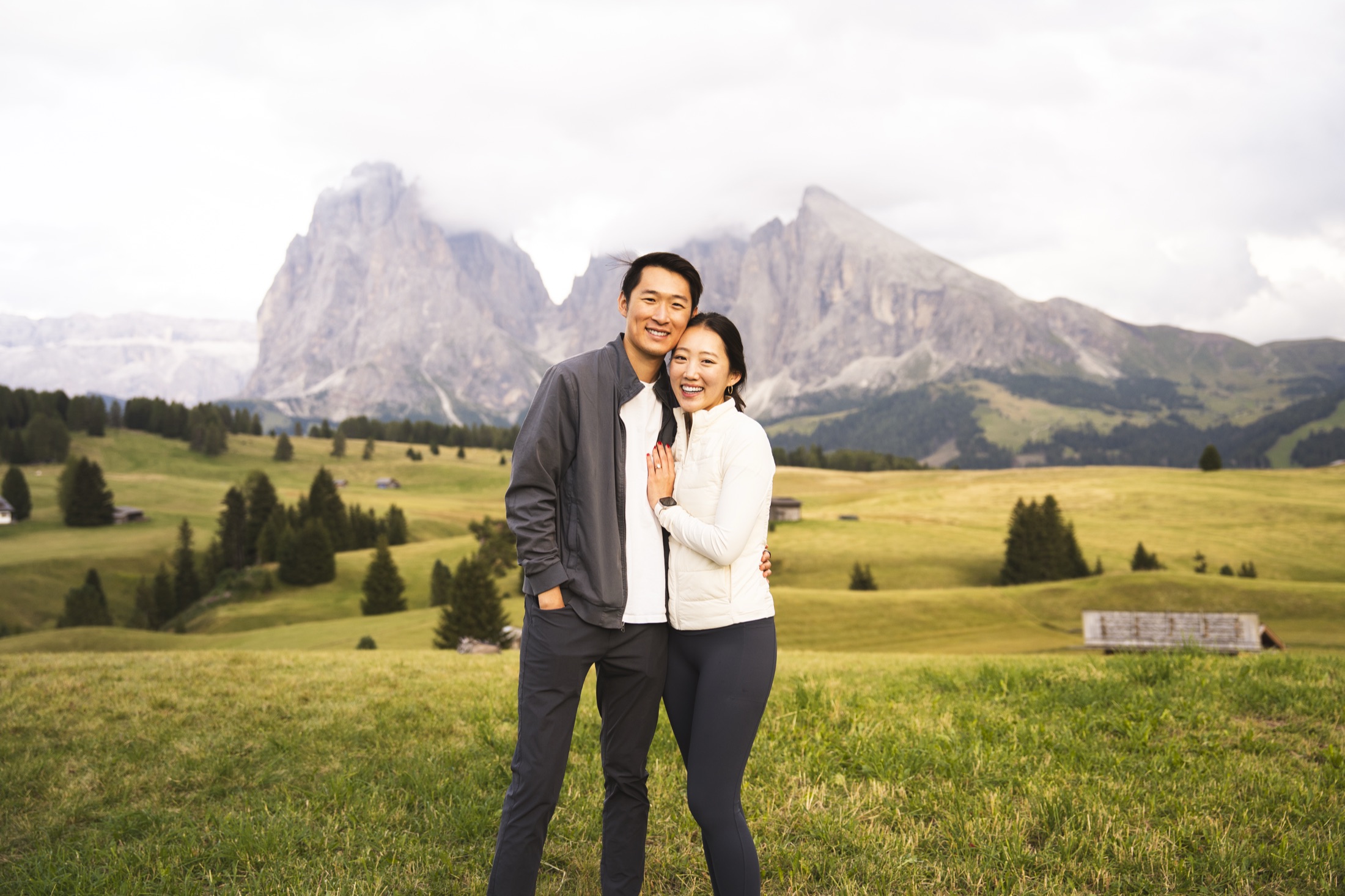 Sarah and Maurice laughing together in an alpine meadow at Alpe di Siusi, the peaks of the Dolomites rising behind them